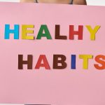 A woman holds a pink poster with colorful letters spelling 'HEALTHY HABITS'.